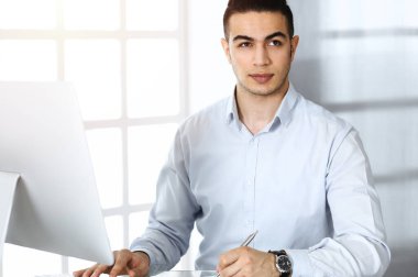 İşadamı güneşli ofiste bilgisayarla çalışıyor. Arap erkek girişimcinin iş yerindeki vesikalığı
