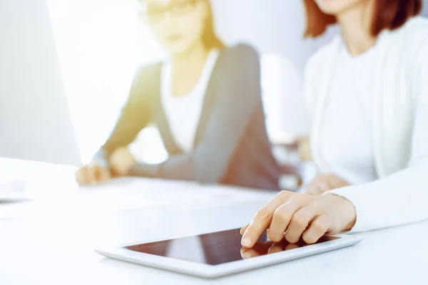 Businesswoman pointing at tablet computer screen while giving presentation to her female colleague. Group of business people working at the desk in office. Teamwork concept