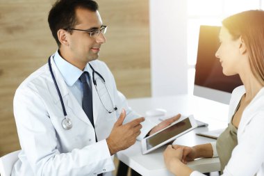 Doktor ve hasta güneşli klinikteki masada otururken tıbbi muayene sonuçlarını tartışıyorlar.