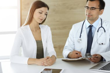 Doktor ve hasta güneşli klinikteki masada otururken tıbbi muayene sonuçlarını tartışıyorlar.