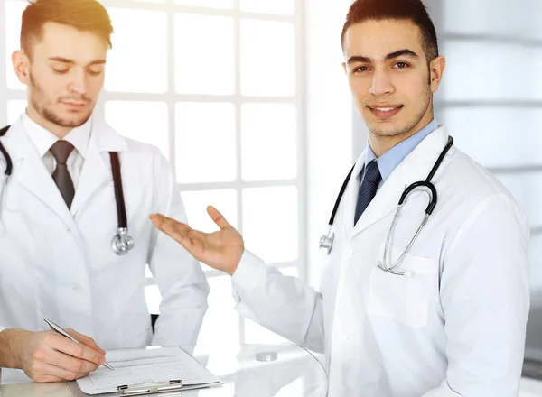 Arabische arts die aan het glazen bureau zit met een blanke collega in een medisch kantoor of een zonnige kliniek. Diverse artsen team, medisch concept — Stockfoto