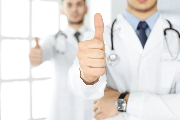 Два врача-мужчины, стоящие в одной команде с большими пальцами в больничном кабинете и готовые помочь пациентам. Медицинская помощь, лучшее лечение заболеваний и концепция медицины — стоковое фото