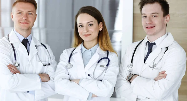 Bir grup modern doktor hastane ofisinde kollarını kavuşturmuş bir takım gibi duruyorlar. Doktorlar hastaları muayene etmeye ve yardım etmeye hazır. Tıbbi yardım, sağlık sigortası, en iyi tedavi ve ilaç — Stok fotoğraf