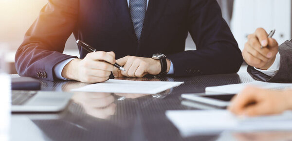 Unknown business people working together at meeting in modern office, close-up. Businessman and woman with colleagues or lawyers discussing contract at negotiation