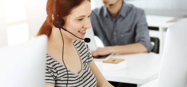 İnternette müşterilerle konuşurken kulaklık ve bilgisayar kullanan sıradan giyinmiş genç bir kadın. Güneşli ofiste çalışan bir grup operatör. Çağrı merkezi