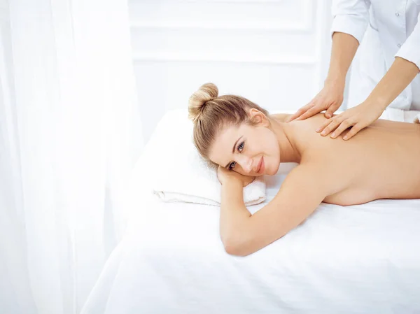 Jonge en blonde vrouw geniet van massage van rug in spa salon. Schoonheidsconcept — Stockfoto