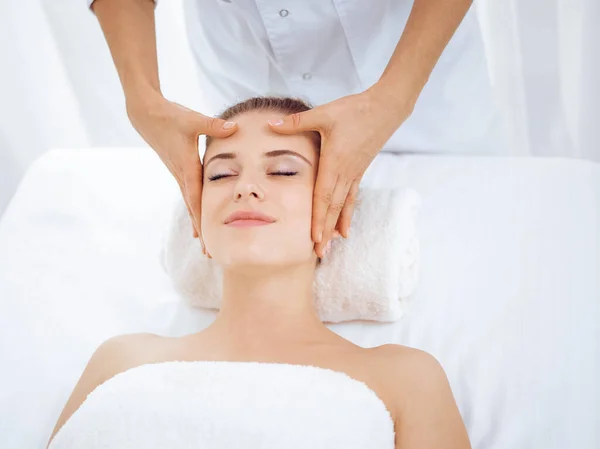 Young and blonde woman enjoying facial massage in spa salon. Beauty concept Stock Picture