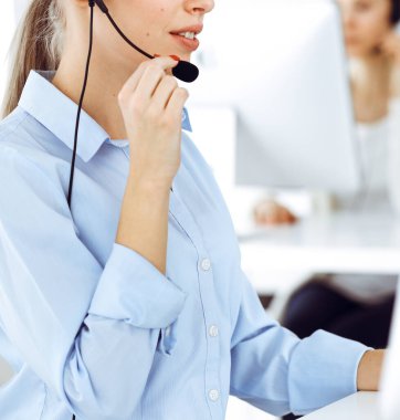 Kadın çağrı operatörü çevrimiçi ve yakın çekim müşterilerine danışmak için bilgisayar ve kulaklık kullanıyor. Müşteri hizmetleri işgali olarak çalışan çeşitli kişiler grubu