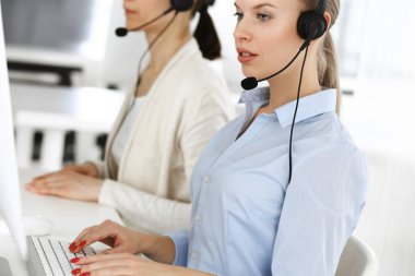 Sarışın kadın çağrı operatörü müşterilere danışmak için bilgisayar ve kulaklık kullanıyor. Müşteri hizmetleri işgali olarak çalışan bir grup insan. İş konsepti