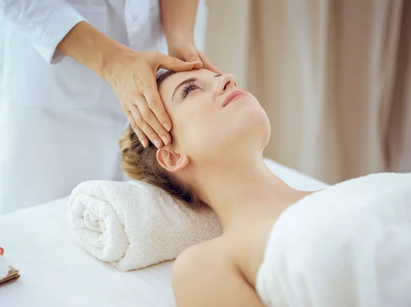 Jonge en blonde vrouw geniet van gezichtsmassage in spa salon. Schoonheidsconcept — Stockfoto