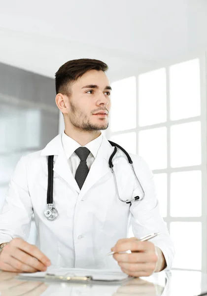 Doctor hombre llenando el formulario de registros de historial de medicamentos mientras está sentado en el escritorio de cristal en la clínica. Concepto de medicina y salud — Foto de Stock