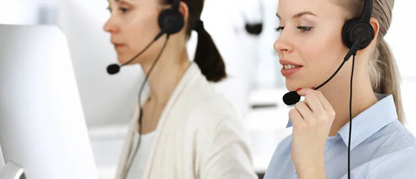 Blond woman call operator is using computer and headset for consulting clients online. Group of diverse people working as customer service occupation. Business concept