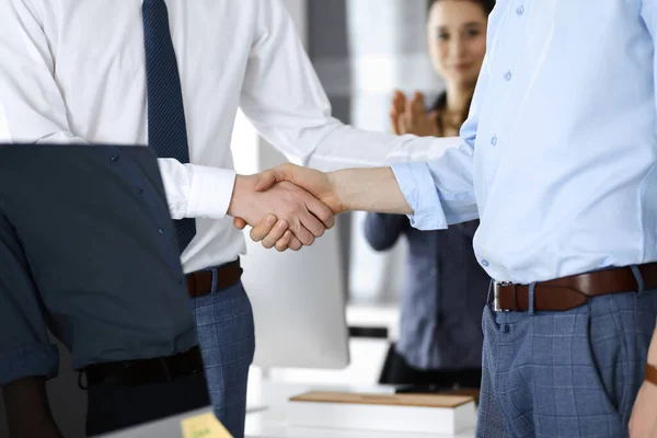 2人のビジネスマンのオフィスで、クローズアップ握手している。背景には手を挙げて幸せと興奮のビジネスウーマンが立っています。ビジネス界の概念 — ストック写真