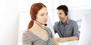 İnternette müşterilerle konuşurken kulaklık ve bilgisayar kullanan sıradan giyinmiş genç bir kadın. Güneşli ofiste çalışan bir grup operatör. Çağrı merkezi