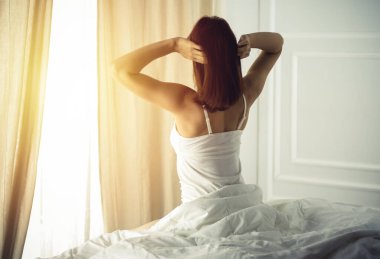 Bir kadın uyandıktan sonra yatakta geriniyor, geriye bakıyor, bir güne mutlu ve rahat giriyor iyi bir gece uykusundan sonra. Esmer için günaydın ve yeni bir gün. Hafta sonu kavramı, tatiller