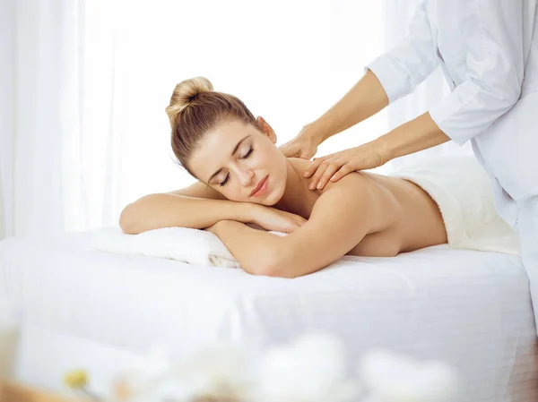 Young and blonde woman enjoying massage of back in spa salon. Beauty concept — Stock Photo, Image