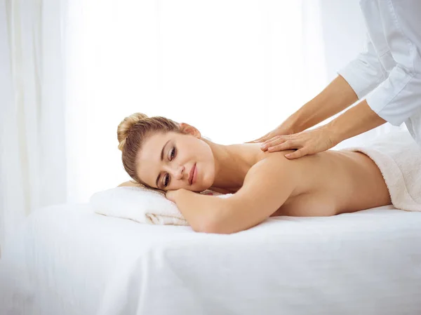 Young and blonde woman enjoying massage of back in spa salon. Beauty concept — Stock Photo, Image