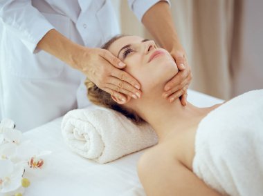 Genç ve sarışın kadın spa salonunda yüz masajından zevk alıyor. Güzellik konsepti