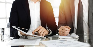 İş adamları güneşli ofiste çalışırken tablet bilgisayar kullanıyorlar. Bilinmeyen bir işadamı ortağıyla masada oturuyor.