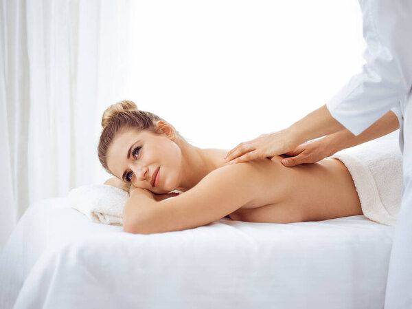 Young and blonde woman enjoying massage of back in spa salon. Beauty concept