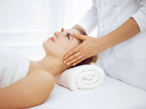 Young and blonde woman enjoying facial massage in spa salon. Beauty concept — Stock Photo, Image