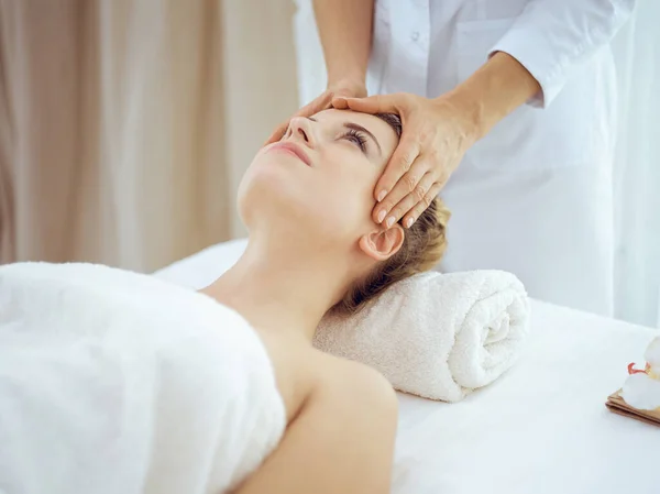 Jonge en blonde vrouw geniet van gezichtsmassage in spa salon. Schoonheidsconcept — Stockfoto