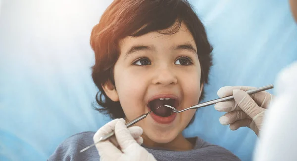 Cute arab boy sitting at dental chair with open mouth during oral checking up with doctor. Visiting sunny dentist office — Stock Photo, Image