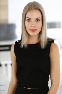 Genç sarışın iş kadını modern ofiste dimdik ayakta duruyor. İş adamları konsepti. Bu portrede siyah elbise ona çok yakışıyor.