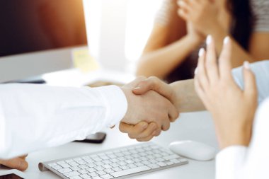 Güneşli ofiste el sıkışan iki işadamı, yakın plan. Meslektaşların başarıyı alkışlaması sona ermiştir.