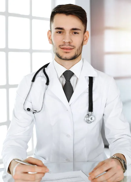 Arzt füllt Krankenakte aus, während er am gläsernen Schreibtisch in der Klinik sitzt. Medizinkonzept — Stockfoto