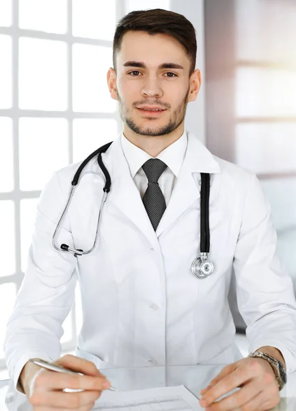 Dokter man vullen medicatie geschiedenis administratie formulier tijdens het zitten aan het glazen bureau in zonnige kliniek. Geneesmiddelenconcept — Stockfoto