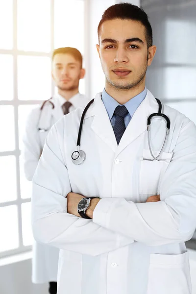 医務室や診療所で白人の同僚と一緒に立っているアラブの医師の男。多様な医師チーム、医療およびヘルスケアの概念 — ストック写真