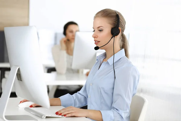 Blond woman call operator is using computer and headset for consulting clients online. Group of diverse people working as customer service occupation. Business concept