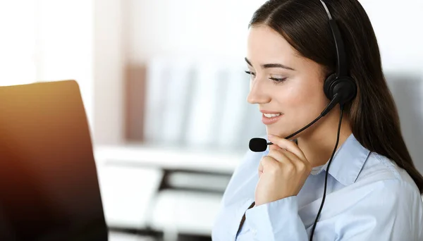 브루넷 여성 고객 서비스 대표는 헤드셋을 사용하고 온라인상에서 고객을 컨설팅 한다. 콜 센터 — 스톡 사진