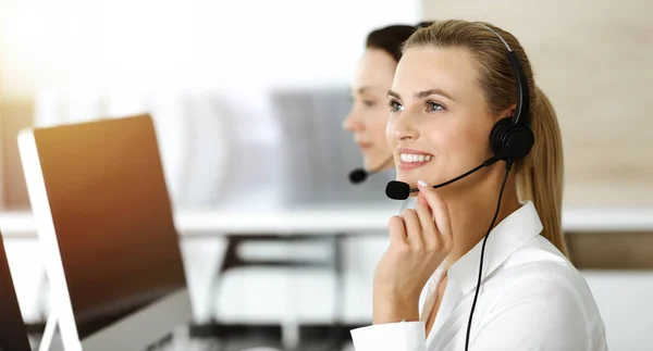 Blond kvinnlig kundtjänst representant konsulterar kunder online med headset i soligt kontor. Begreppet callcenter — Stockfoto