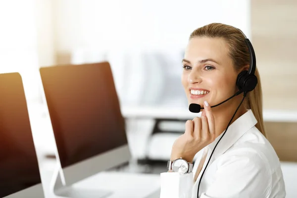Blond žena zástupce zákaznického servisu konzultuje klienty on-line pomocí sluchátek ve slunné kanceláři. Koncept call centra — Stock fotografie