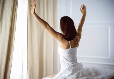 Bir kadın uyandıktan sonra yatakta geriniyor, geriye bakıyor, bir güne mutlu ve rahat giriyor iyi bir gece uykusundan sonra. Esmer için günaydın ve yeni bir gün. Hafta sonu kavramı, tatiller