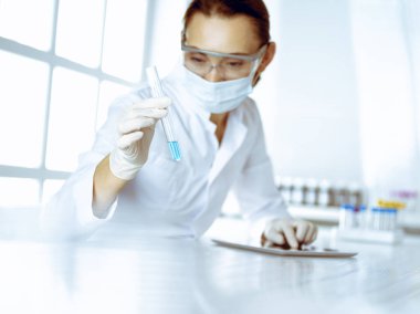 Kadın laboratuvar asistanı mavi sıvıyla test tüpünü analiz ediyor. Tıp, sağlık ve araştırma konsepti