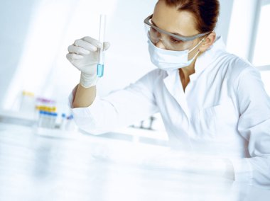 Kadın laboratuvar asistanı mavi sıvıyla test tüpünü analiz ediyor. Tıp, sağlık ve araştırma konsepti