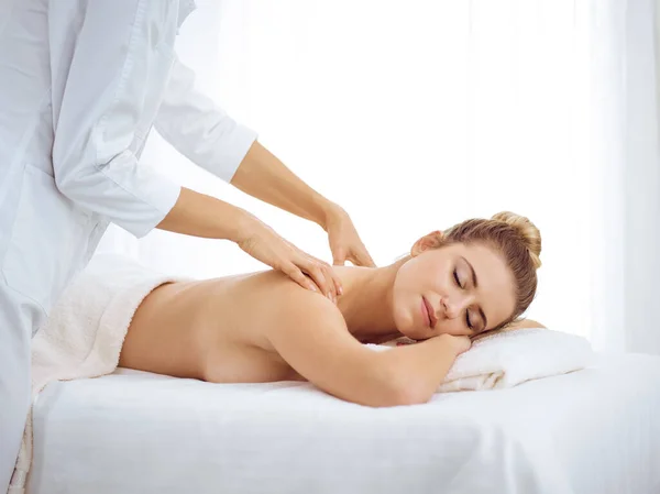 Young and blonde woman enjoying massage of back in spa salon. Beauty concept — Stock Photo, Image