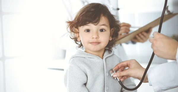 Γυναίκα-γιατρός εξετάζει ένα παιδί ασθενή με στηθοσκόπιο σε ηλιόλουστο κλινικό. Χαριτωμένο Αραβικό νήπιο σε ραντεβού με γιατρό — Φωτογραφία Αρχείου