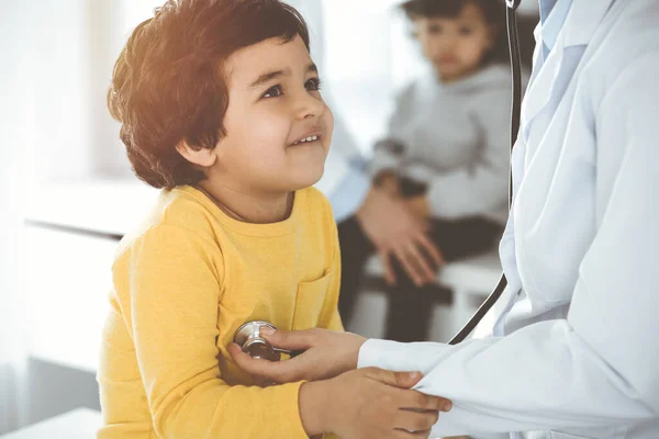 Mujer-médico examinando a un niño paciente por estetoscopio en el soleado Clinik. Lindo chico árabe en la cita con el médico — Foto de Stock