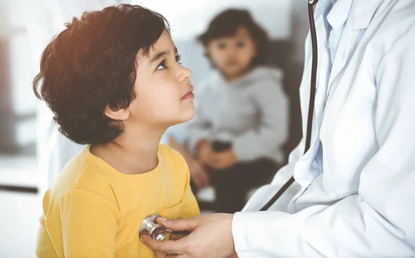 Mujer-médico examinando a un niño paciente por estetoscopio en el soleado Clinik. Lindo chico árabe en la cita con el médico — Foto de Stock