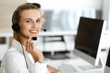 Sarışın kadın müşteri hizmetleri temsilcisi ve meslektaşı internetteki müşterilerine kulaklık kullanarak danışıyorlar. Çağrı merkezi ve iş adamları kavramı