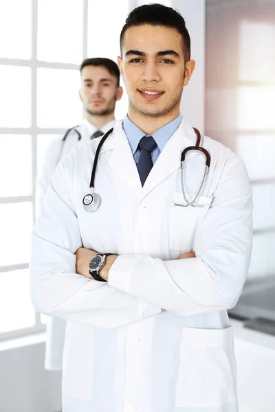 Medico arabo in piedi con collega caucasico in studio medico o in clinica. Diversi medici team, medicina e concetto di assistenza sanitaria — Foto Stock