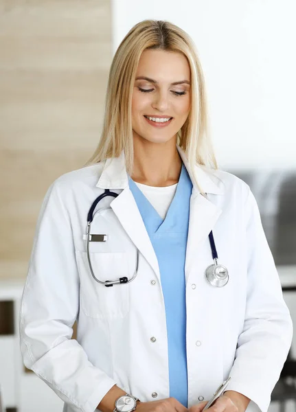 Nő-orvos a klinikán, boldog a szakmájával. A szőke női orvos ellenőrzi a kórtörténetét és az orvosi vizsgálat eredményeit. Orvosi fogalom — Stock Fotó