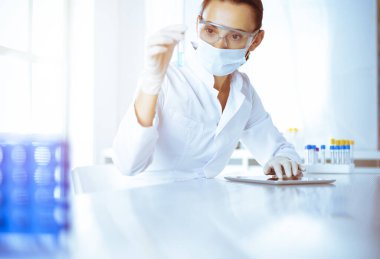 Kadın laboratuvar asistanı mavi sıvıyla test tüpünü analiz ediyor. Tıp, sağlık ve araştırma konsepti