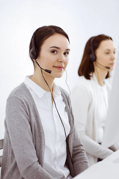 Centro de llamadas. Mujer vestida casual trabajando en auriculares con diversos colegas en la oficina. Concepto empresarial —  Fotos de Stock