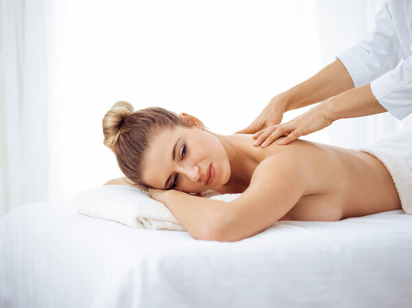 Young and blonde woman enjoying massage of back in spa salon. Beauty concept