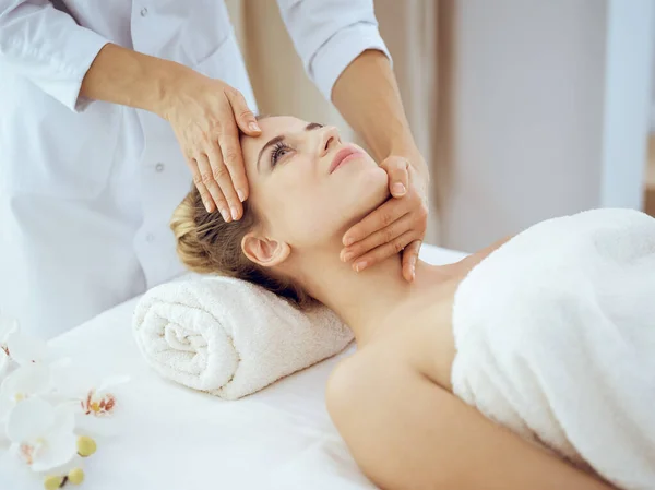 Jonge en blonde vrouw geniet van gezichtsmassage in spa salon. Schoonheidsconcept — Stockfoto